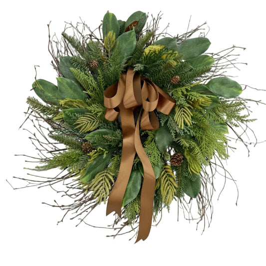 Green wreath with a brown ribbon hanging on a tree in a snowy forest.