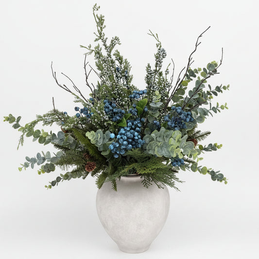 Decorative wreath with greenery and berries on a metal gate with snow-covered ground and trees in the background.