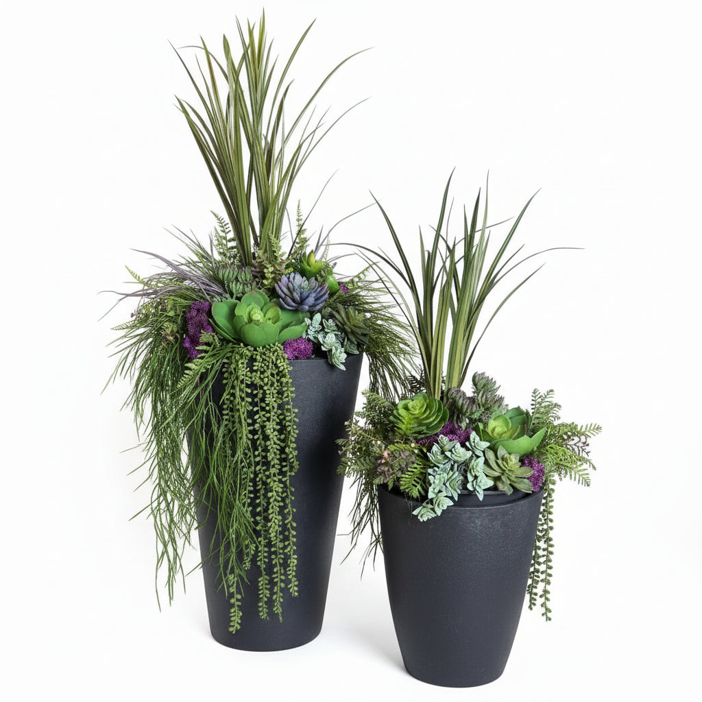 Two black planters with greenery and purple flowers on a textured surface.