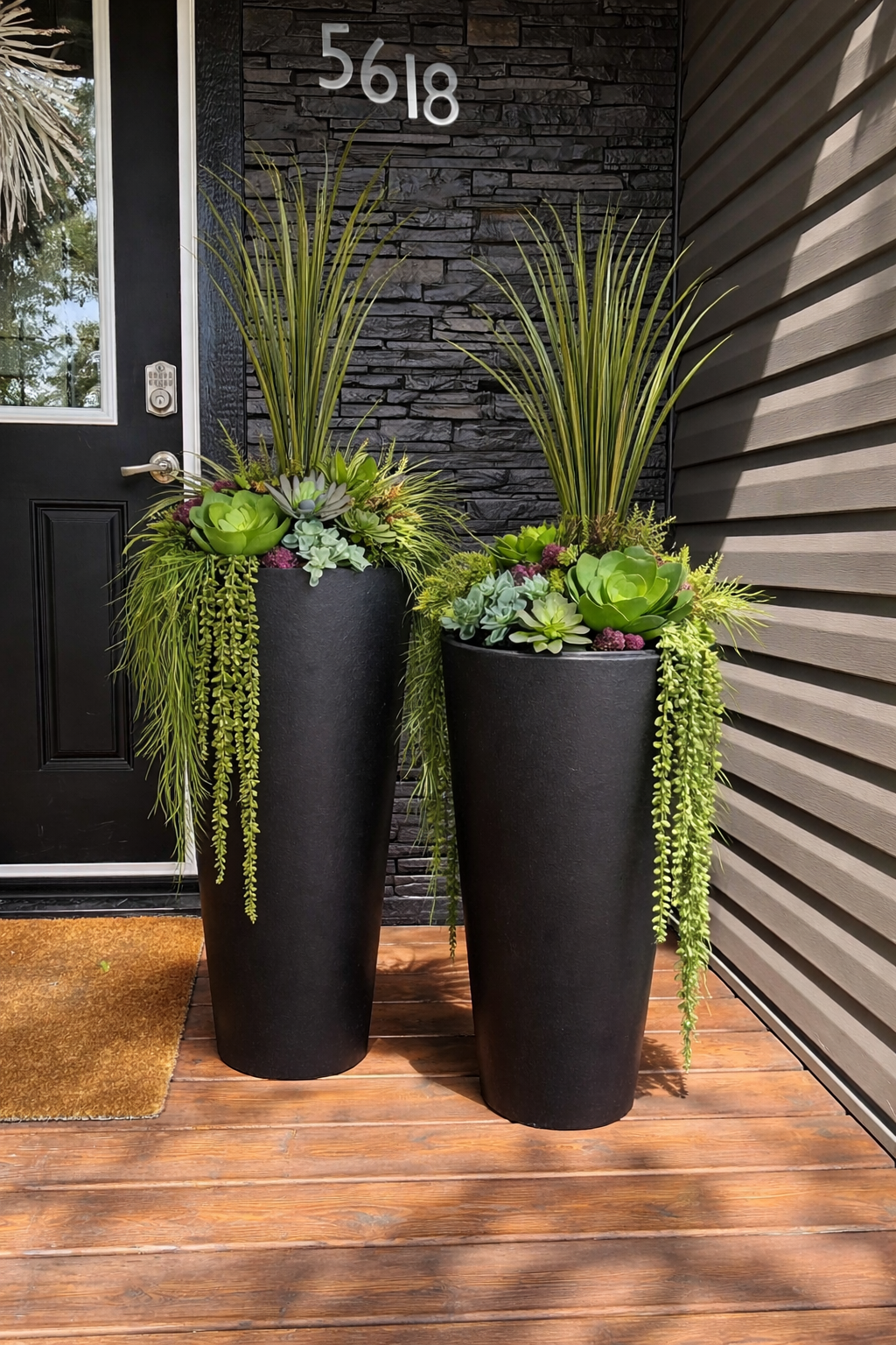 Two black planters with greenery and purple flowers on a textured surface.