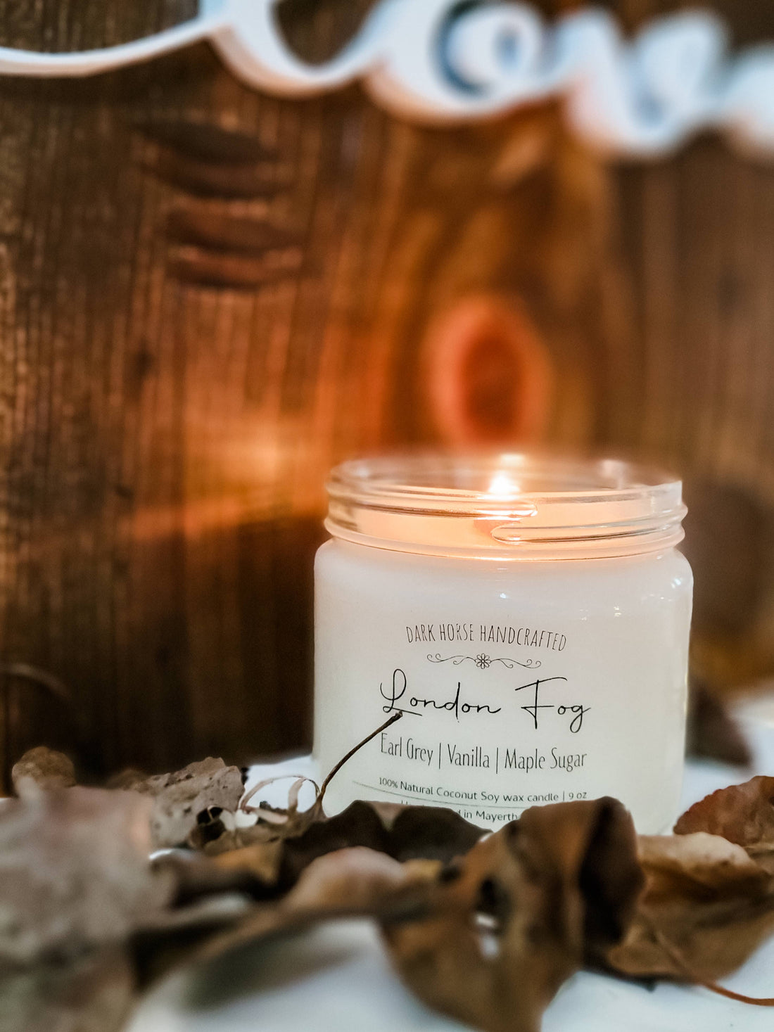 London Fog soy candle burning warmly beside dried autumn leaves