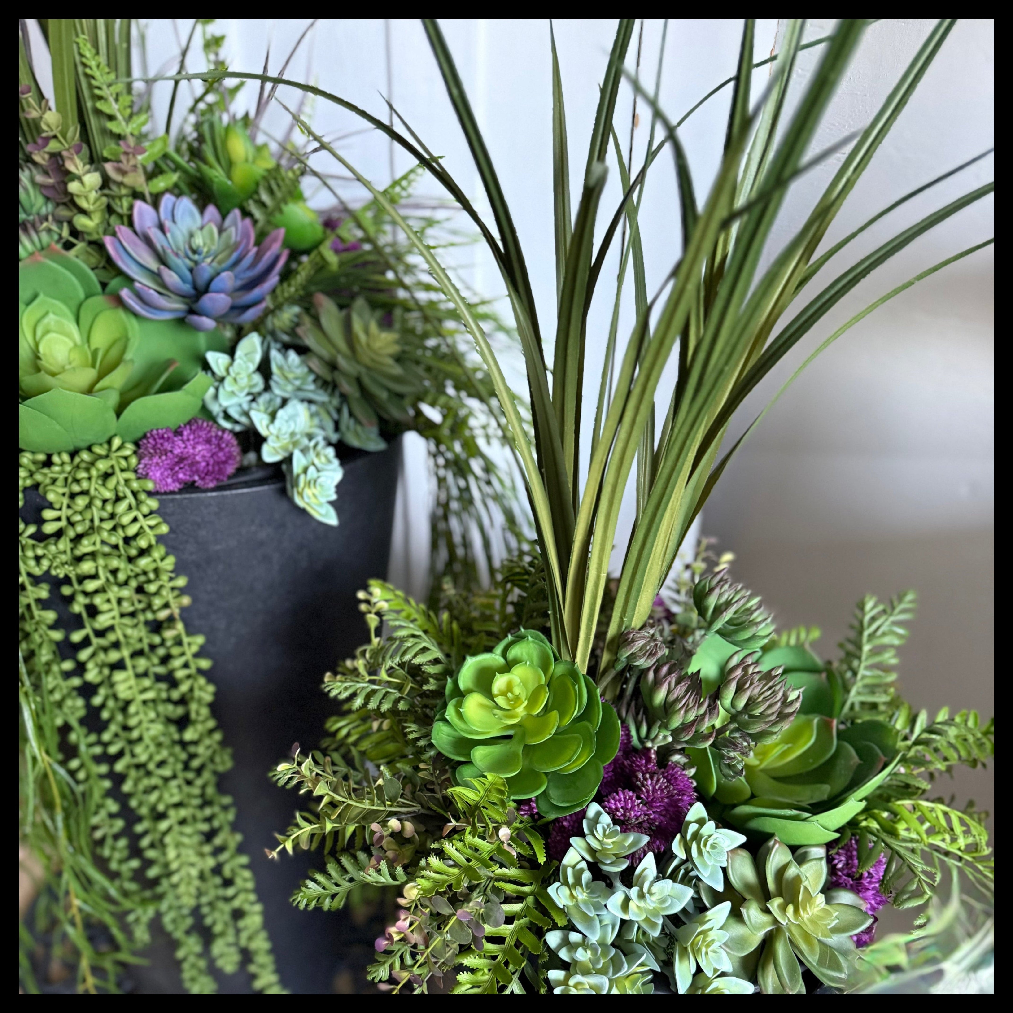 Decorative arrangement of artificial plants in gray pots on a neutral surface.